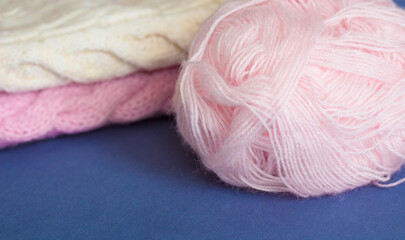 Fototapeta na wymiar Knitting with needles, ball of pink yarn, knitted clothes on a blue background
