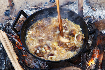 Pieces of lamb with onion are fried in boiling oil on the fire. As a stage in the preparation of traditional pilaf.