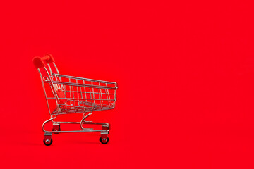 Shopaholic shopper concept.Close up view of one single shine tiny toy shopping cart on a bright red background. Empty push cart with copy space on right. Sale, discount, holiday shopping for ads.