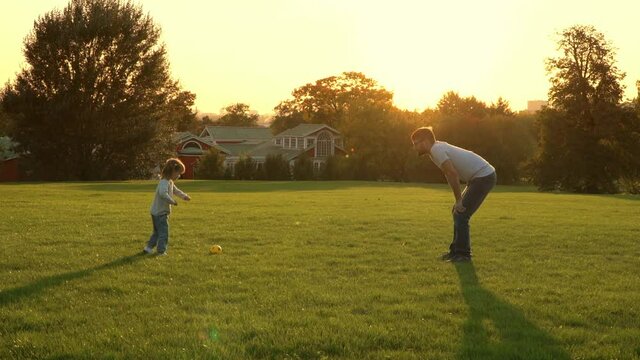 Young father and little girl play to tball in summer park at sunset. Happy family weekend and sports outdoors concept. Father plays with child in nature.