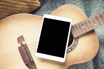 Acoustic guitar and digital tablet on a couch at cozy home background. Online music lessons, learning playing or writing songs and hobby concept. Top view, flat lay, mock up