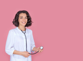 Portrait of a beautiful positive woman doctor, in uniform, with a stethoscope. The concept of the presentation of the clinic. Isolate on a pink background. Copy space