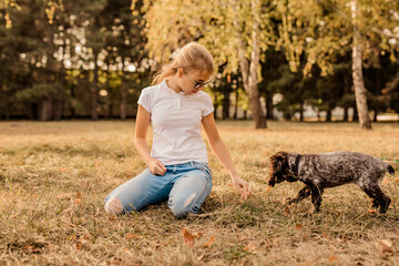 Young girl 12 years old in glasses, white shirt and jeans walking with her little dog spaniel,...