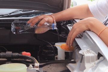 Women refills windshield wiper water on a car.