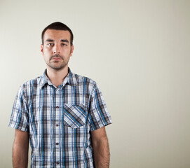 Obraz premium Studio photo of dark haired man with a short sleeved checkered shirt on a light brown beige background.