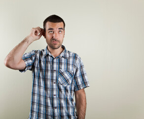 Studio photo of dark haired man looking confused with a short sleeved checkered shirt on a light brown beige background.