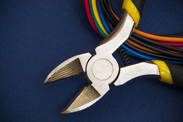Wire cutters or diagonal pliers and wires close up on dark blue background