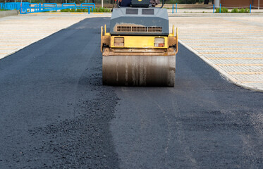 Worker leads the vibrating road roller to compact the asphalt laid out for the construction of a road