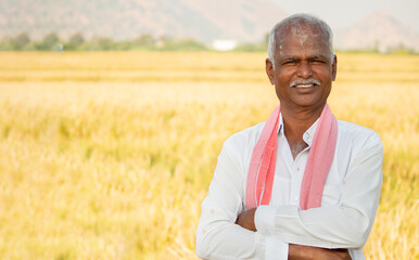 Portrait of Confident smiling Indian farmer with arms crossed standing in front of agriculture...