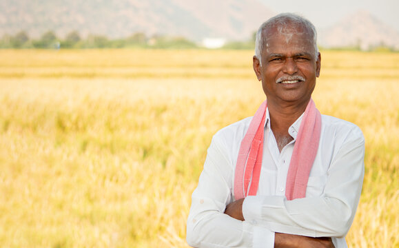 Portrait of Confident smiling Indian farmer with arms crossed standing in front of agriculture farmland looking camera with copy space.