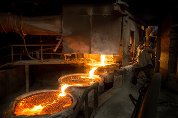 Steelworker at work near arc furnace and pouring liquid metal 