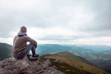 young strong man sitting on the rock at the top of the mountains peak