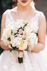 The bride holds a wedding bouquet of light-colored roses in her hands