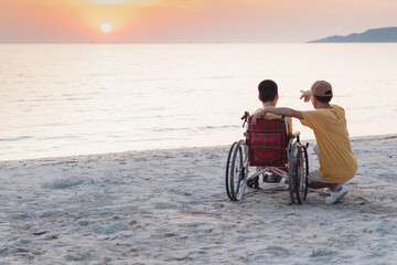 Naklejka premium Father​ and Asian special child on wheelchair playing, doing activity on sea beach in summer, Lifestyle of disability child, Life in the education age, Happy disabled kid in travel holidays concept.