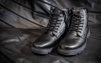 Black boots made of genuine leather. Men's winter shoes with laces, fashionable style. On a dark leather background.