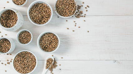 Hemp seeds in small white bowls and spoon on white wooden table. Set of small bowls with raw...