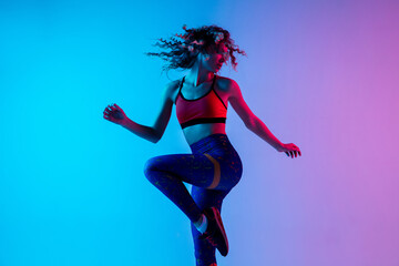 Fototapeta na wymiar Sport dancing. Beautiful woman in bright sportwear isolated on gradient pink-blue background in neon light. Athletic and graceful. Modern sport, action, motion, youth concept. Female practicing