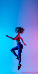 Jump. Young beautiful woman in bright sportwear isolated on gradient pink-blue background in neon light. Athletic and graceful. Modern sport, action, motion, youth concept. Sportive female practicing