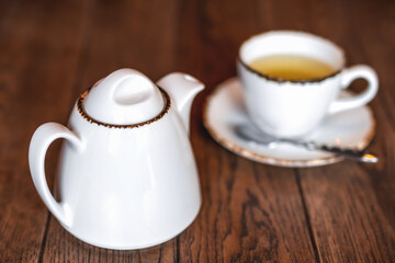 Fototapeta premium White ceramic teapot and a Cup of invigorating fresh fragrant tea on a brown wooden table.