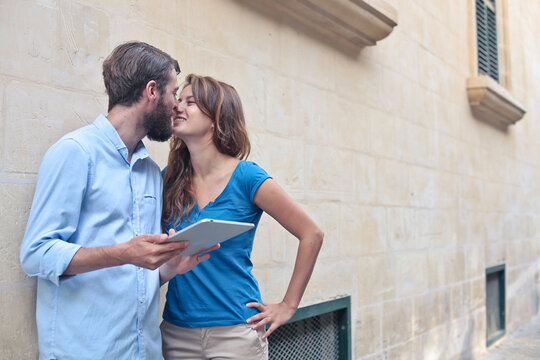 young couple leaning against a wall uses a tablet