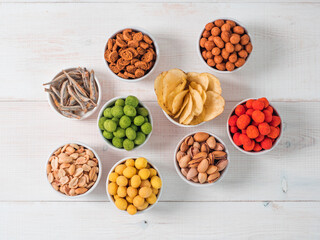 Assortment of different snack for beer, wine, party. Peanuts in coconut glaze, green vasabi, red spicy chilli, yellow cheese glaze, chips, pistachio, crackers, fish on white wooden table. Copy space