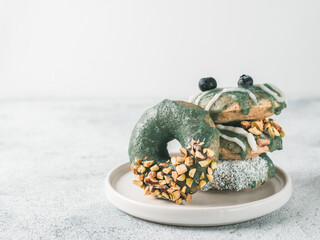 Vegan doughnuts with chia seeds topped with healthy spirulina glaze with pistachio, desiccated coconut and blueberry. Stack of blue green spirulina donuts on gray background. Copy space.