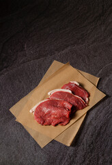 Low key shot of three halal meat fresh raw beef filets on baking paper on a blackboard background illuminated by a single light source with black negative space in the upper half area.