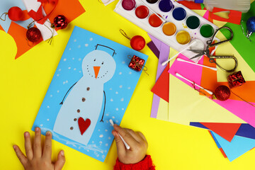The child makes a Christmas card on the table of the house, applique snowman