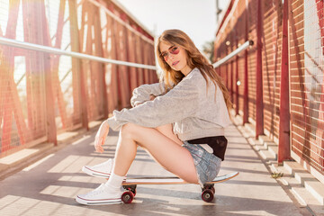 Skater girl sitting on a skateboard. Portraits of a young woman with a longboard
