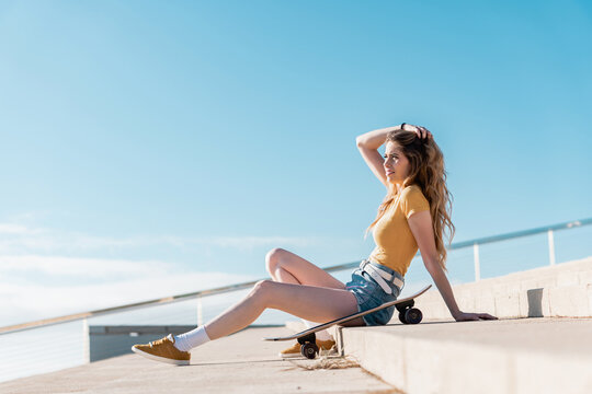 Long board girl sitting on the stairs outdoors with a skateboard in summer. Sunny day for outside activities. Cool California concept