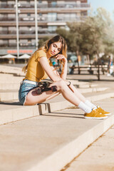 Long board girl sitting on the stairs outdoors with a skateboard in summer. Sunny day for outside activities. Cool California concept