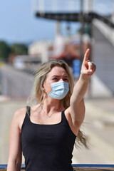 a woman wearing a surgical mask and a tank top pointing upwards