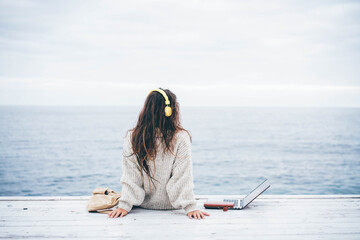 Young woman using laptop computer and listening music near winter sea. Freelance work concept