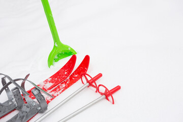 Children's red skis with sticks and a green snow shovel-layout in the snow. Winter outdoor activities, family fun. White natural frosty background. Copy space