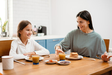 Obraz na płótnie Canvas Cheerful beautiful mother and daughter smiling while having breakfast
