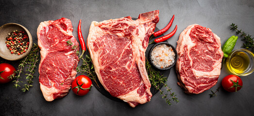 Variety of Fresh Raw Black Angus Prime Meat Steaks T-bone, New York, Ribeye and seasoning on gray background, top view