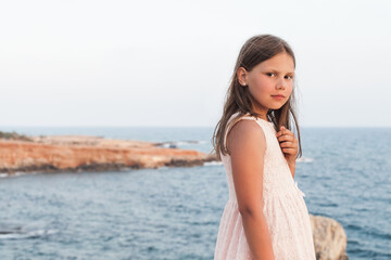Fototapeta na wymiar Little girl in white dress standing at the sea coast