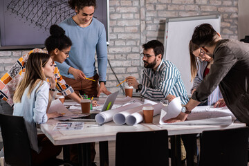 Group of modern business people in casual wear discussing architectural designs while sitting in the creative office.