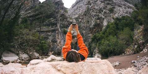 A woman lies on a large stone and takes a selfie on a smartphone.