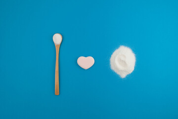 Levocarnitine or L-carnitine powder in bamboo spoon on blue background. Flat lay, top view, copy space