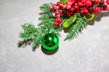 Christmas fir tree branches with green ball, red rowan berries on grey background. Flat lay, top view. Copy space