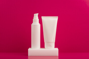 Set of cosmetic bottles on white podium against pink background
