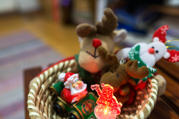 Fototapeta na wymiar Colorful Christmas plush animals and snowman toys in a wooden basket, focus on the led illuminated snowman.