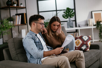 Worried couple paying their bills online with laptop at home in the living room. Couple having...