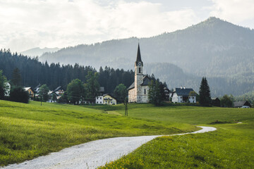 Fototapeta premium Road to a traditional picturesque church in Austrian Alps, Europe. Beautiful day in dummer