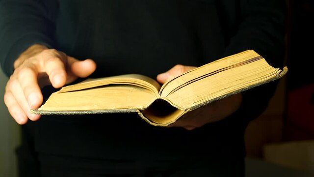 Hands turning old open antique book pages, moving through old literature. Man skimming through a simple retro, vintage thick book, reading concept. Bible, prayer book, dictionary, novel