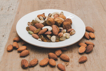 A variety of nuts  are in dish on wooden background at the center of the image, selective focus.