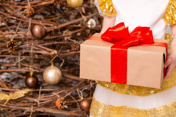 A girl in a chic dress stands with a New Year's gift in her hands against the background of a New...