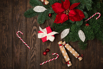Holiday card - red flower poinsettia, Christmas decorations, gift boxes and candy canes on dark wooden background.