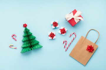 Winter Christmas holiday shopping concept. Craft paper bag, Xmas green tree and gift boxes on blue background.